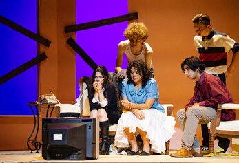 Students gather around a television in a tense scene from Portola High School’s “Night of the Living Dead,” watching intently while seated on a couch.