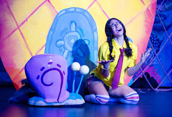 A student performs a solo moment in Portola High School’s “SpongeBob,” singing beside a large snail prop on a brightly colored set.