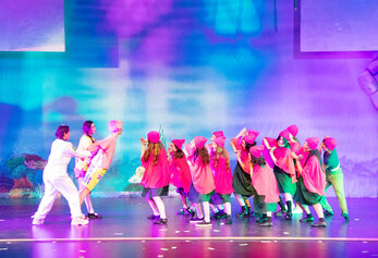 Students perform a group dance number in Portola High School’s “SpongeBob,” wearing coordinated costumes under vibrant, multicolored lighting.